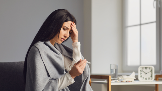 Woman feeling head and looking at a thermometer to see how long a fever lasts