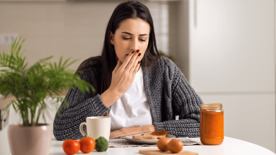 Woman feeling nauseous after eating breakfast, sitting at a table with food