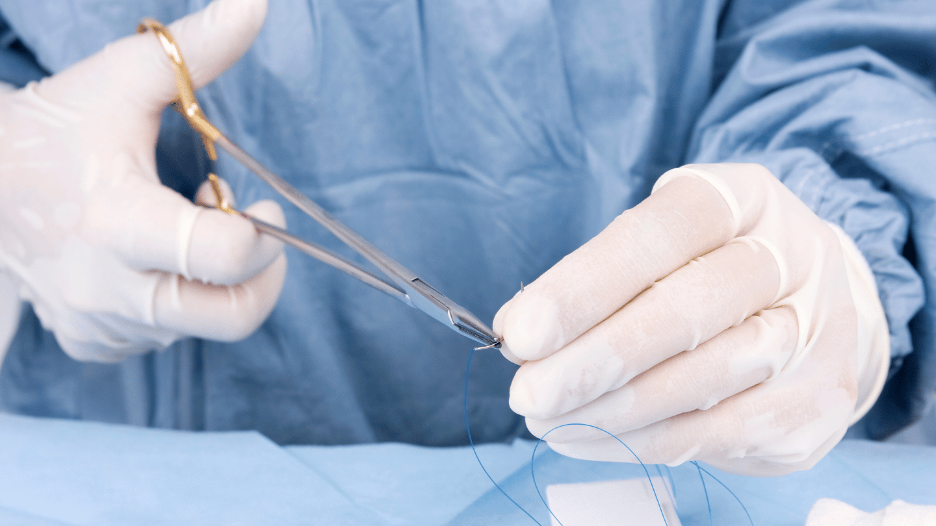 CityMD doctor in surgical gloves holding suturing equipment, preparing to stitch a cut