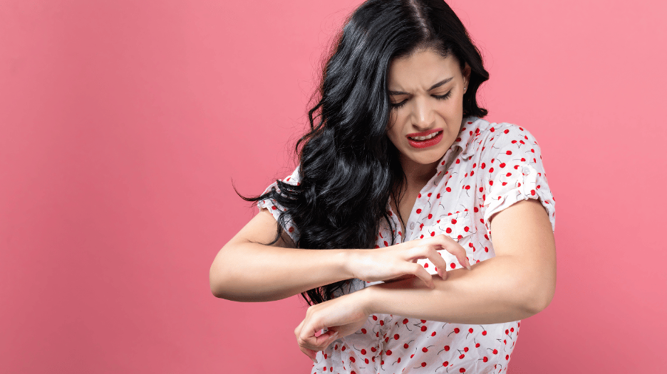 Young woman with a pained expression scratching her arm, showing discomfort from a fever rash