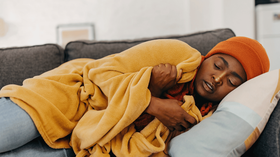 A person bundled in blankets and resting on a couch, illustrating the effects of cold weather and staying warm during winter.