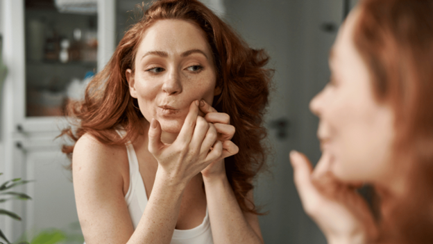 Woman examining a blood blister on her face in a mirror