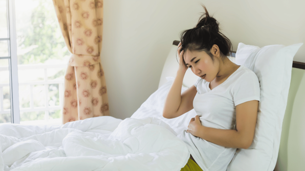 Woman sitting in bed holding her stomach, showing signs of abdominal pain or diarrhea-related discomfort